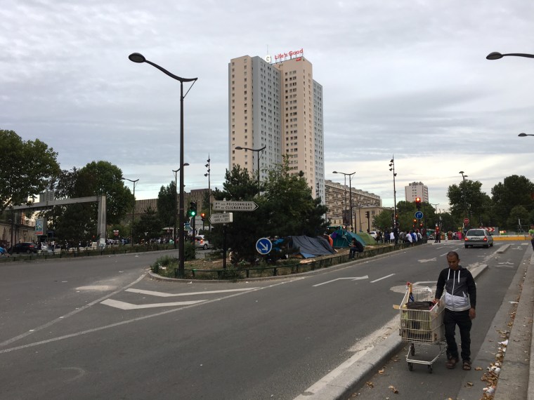 Image: Migrants gather bedding and food at the traffic intersection in Porte de la Chapelle, Paris.