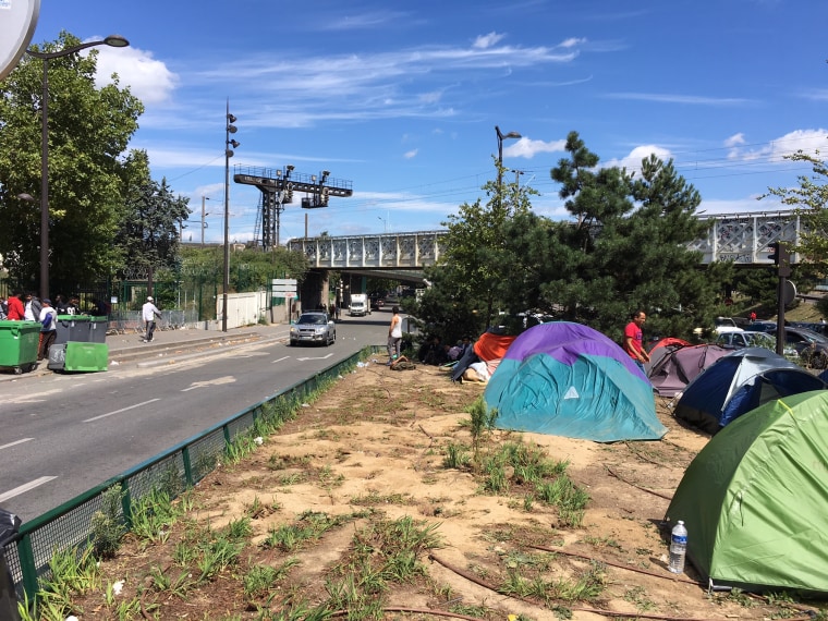 Image: Migrants living in the median between traffic lanes at Porte de la Chapelle, Paris.