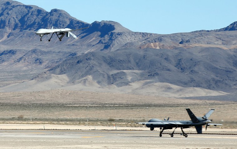 Image: An MQ-1B Predator remotely piloted aircraft (RPA) flies past a MQ-9 Reaper RPA as it taxis during a training mission at Creech Air Force Bas