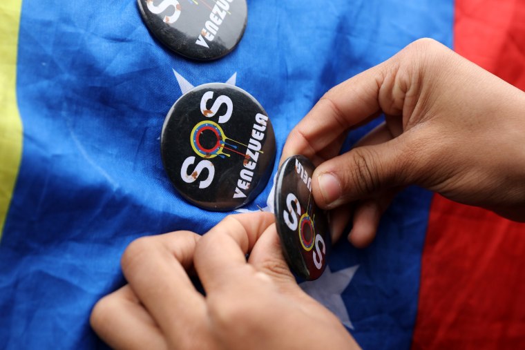 Image: A demonstrator places a badge on a Venezuelan flag at a protest  against Venezuela's President Nicolas Maduro's government during a meeting of foreign affairs ministers and representatives from across the Americas to discuss issues related to the V