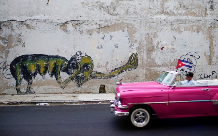 Image: A vintage car passes by a graffiti of Cuban Artist Yulier Rodriguez in Havana, Cuba
