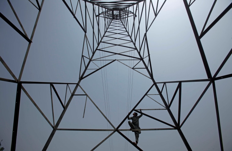 Image: A worker of PESCO climbs up a high-voltage pylon in Peshawar