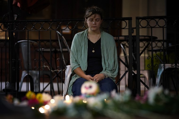 Image: A young woman sits near a makeshift candlelight vigil