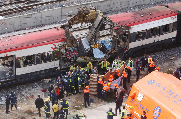 Image: Rescue workers cover up bodies alongside a bomb-damaged passenger train