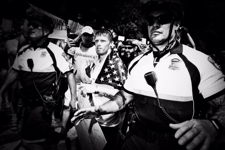 Image: A 'Free Speech Rally' attendee is ushered through the crowd of protesters by police.