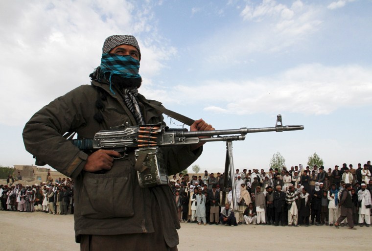 Image: A member of the Taliban and onlookers during the execution of three men in Afghanistan's Ghazni province