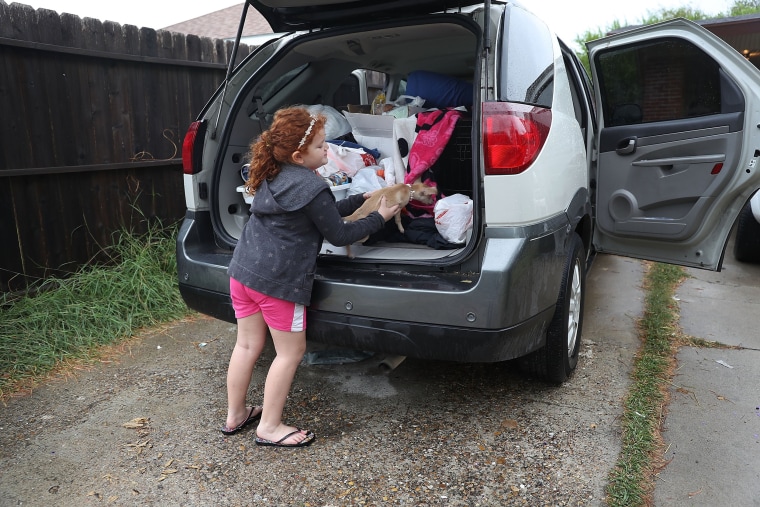 Image: A girl places her dog into the car as her family evacuates their home