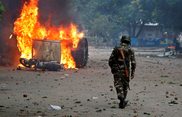 Image: A member of the security forces walks towards a burning vehicles  during violence in Panchkula