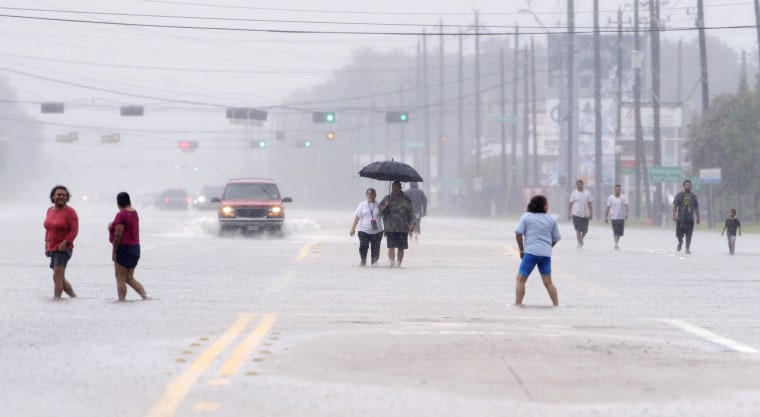 Image: Residents walk along a flooded road as they evacuate neighborhoods in Houston