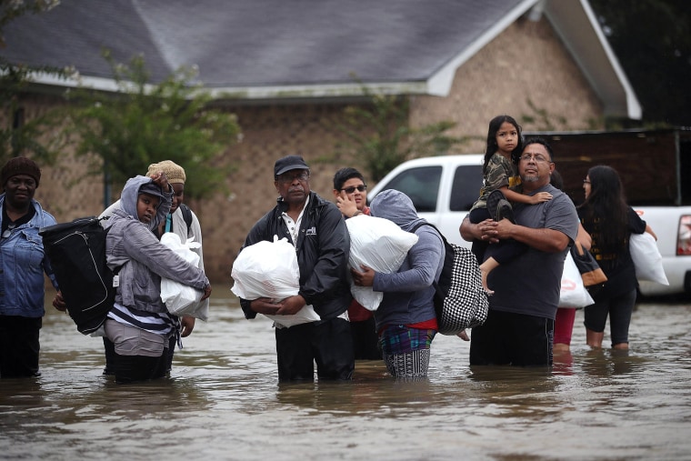 Image: People walk down a flooded street as they evacuate their homes in Houston