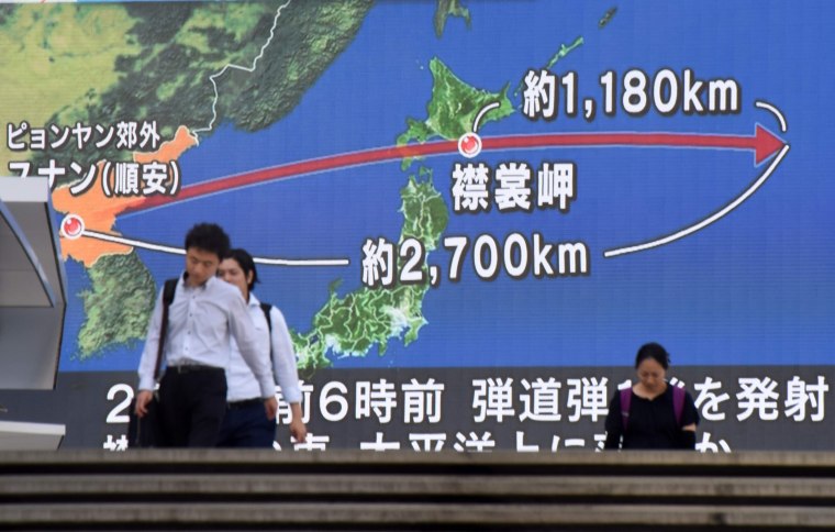 Image: Pedestrians in Tokyo walk past screen showing map of Japan and Korean Peninsula