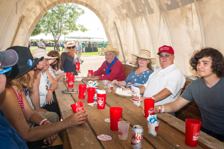 Image: John Mannelly, of Minden, Nevada, at right in white shirt, eats lunch under a covered wagon with friends and family