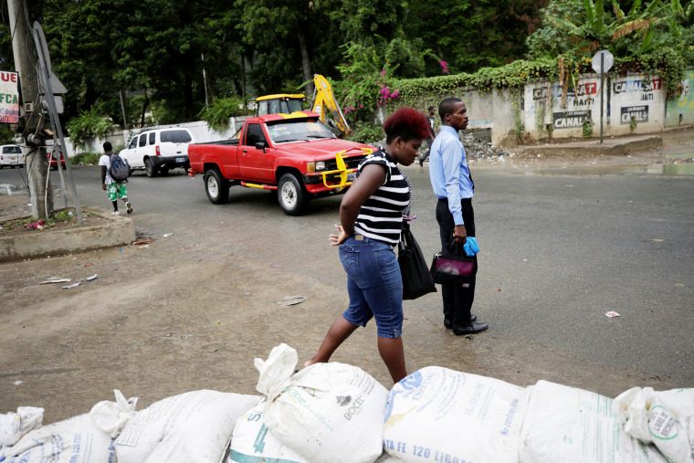 Image: A woman walks past sandbags set in a street of Cap Haitien