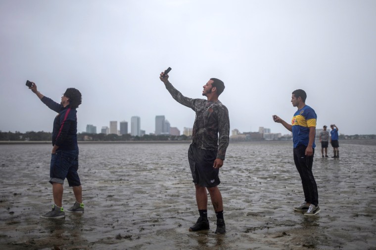 Image: The Tampa skyline is seen in the background as local residents  Rony Ordonez, left, Jean Dejesus and Henry Gallego take photographs after walking into Hillsborough Bay while awaiting the hurricane's arrival in Tampa on Sept. 10.