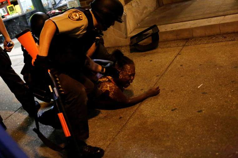 Image: Police officers detain a demonstrator who was pepper sprayed in the face.