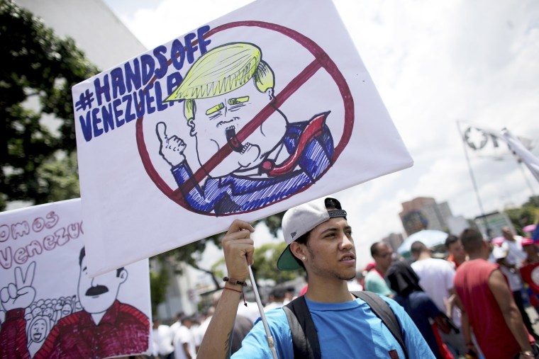 Image: A government supporter holds a placard with the universal "No" symbol over a caricature of U.S. President Donald Trump