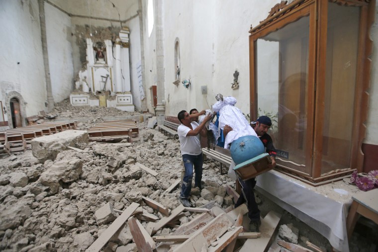 Image: Workers rescue a religious statue from the heavily damaged former convent of San Juan Bautista