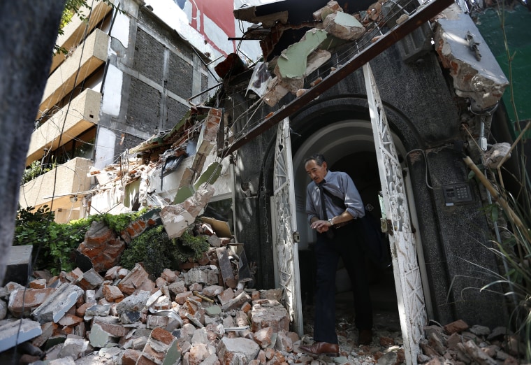 Image: A man walks out of the door frame of a building that collapsed