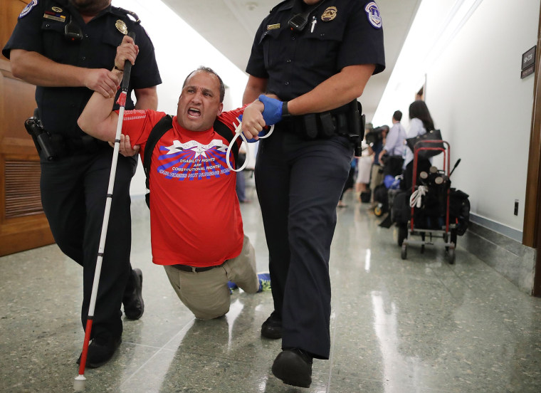 Image: U.S. Capitol Police drag a blind protester out of a Senate Finance Committee hearing