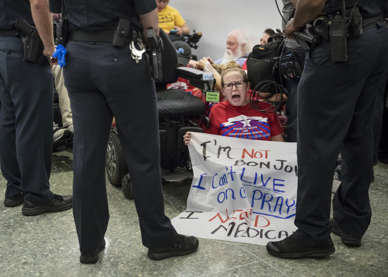 Image: An activist holds a sign that reads, \"I'm not Jon Bon Jovi. I can't live on a prayer. I need Medicaid\"