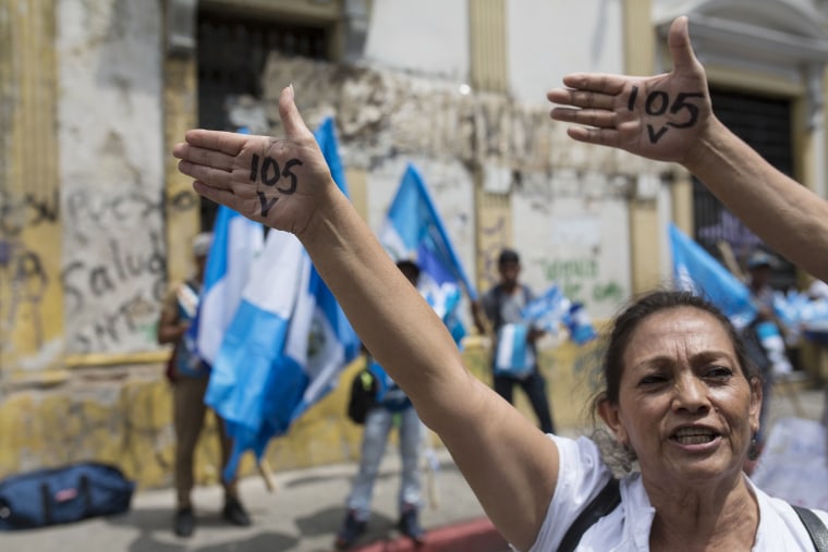 Image: Protesters show their hands with a number "105" in reference to the votes needed in Congress to lift President Jimmy Morales' immunity