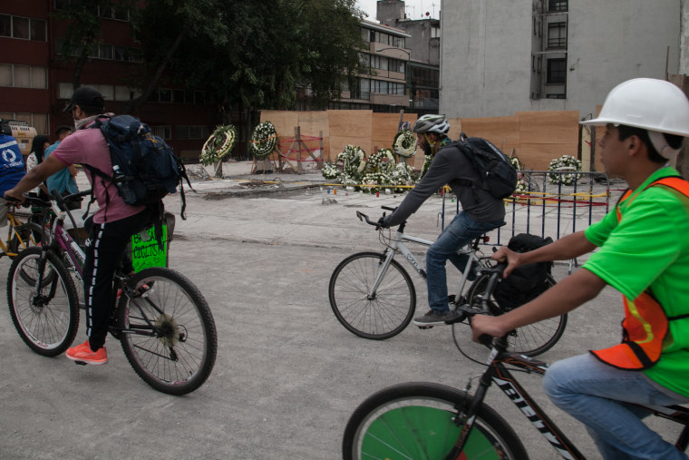 A cyclist brigade passes in front of a razed building where numerous people died following Mexico's devastating earthquake.