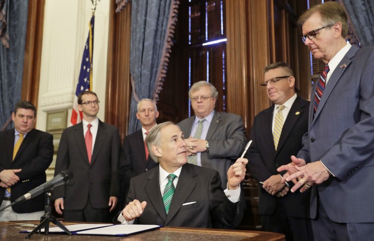 Image: Gov. Greg Abbott, center, offers a pen to Lt. Gov. Dan Patrick, right, after he signed SB7