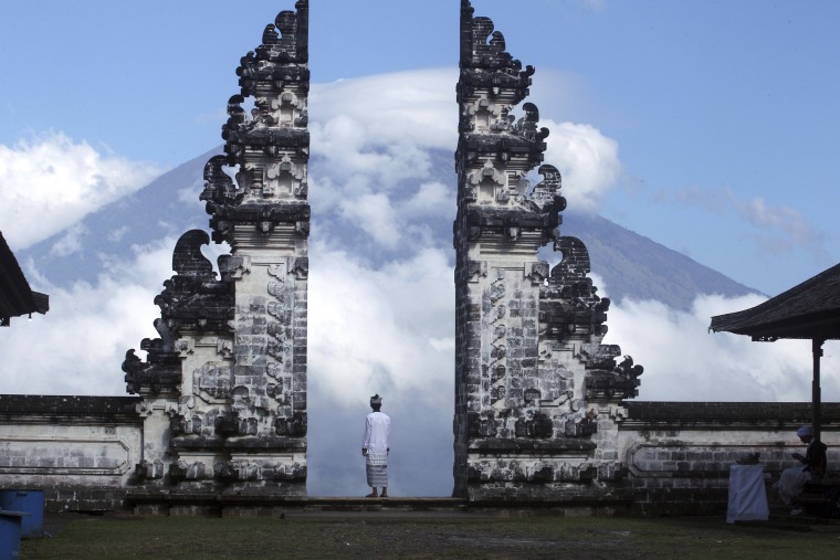 Image: A Balinese man watches the Mount Agung volcano almost covered with clouds as he stands at a temple in Karangasem, Bali