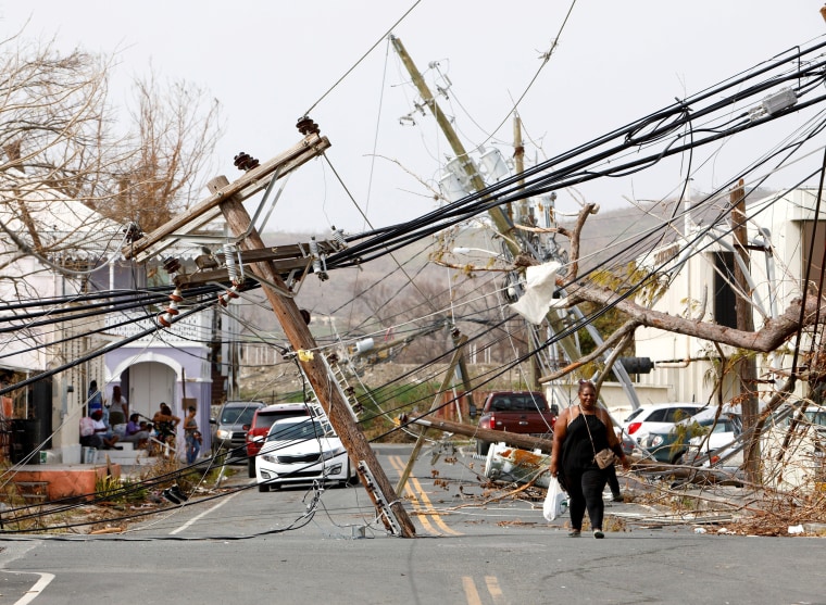 Image: A woman walks on road covered in debris from Hurricane Maria