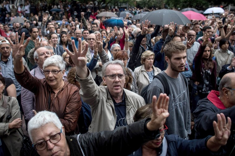 Image: People hold up four fingers representing the four stripes of the Catalan flag while they wait to cast their referendum votes outside the Escola Industrial of Barcelona.