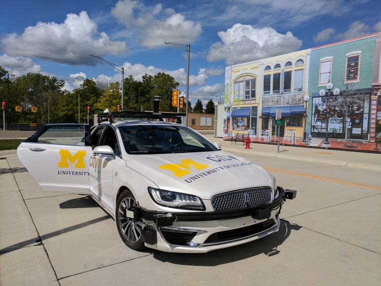 A self-driving car sits in front of a facade of storefronts in Mcity, the University of Michigan's testing facility for autonomous vehicles.