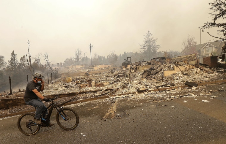 Image: A man rides a bicycle past burned down homes in Santa Rosa