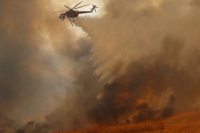 Image: A helicopter drops water on a wind-driven wildfire 