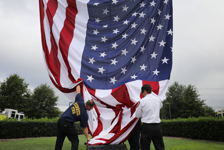 Image: Firefighters raise a U.S. flag ahead of a funeral