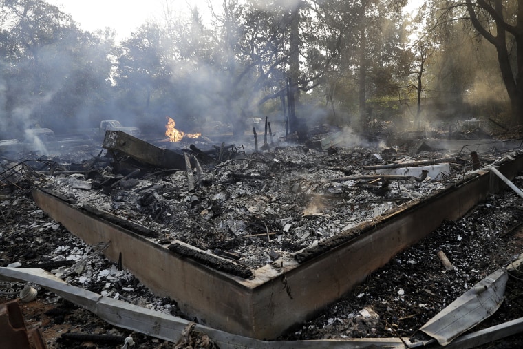 Image: Smoke smolders from a fire-ravaged home destroyed by a wildfire