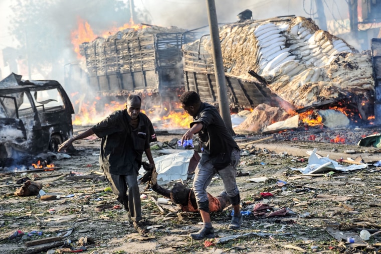 Image: Two men carry the body of a victim following the explosion of a truck bomb