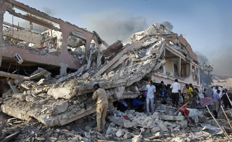 Image: Somalis gather and search for survivors by destroyed buildings at the scene of a blast