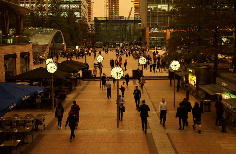 Image: People walk through Canary Wharf while the sky overhead turns red as dust from the Sahara carried by storm Ophelia filters sunlight over London