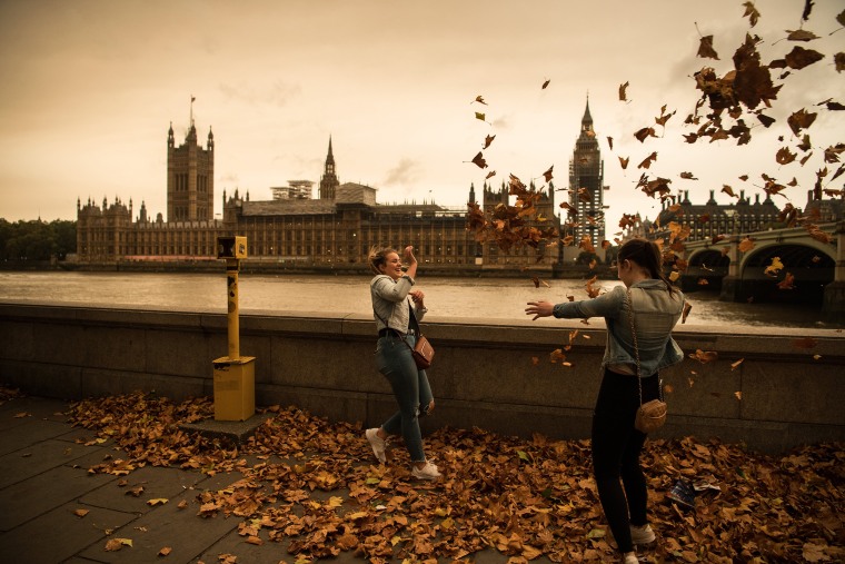Image: Girls throw leaves opposite the Houses of Parliament during a reddish sky caused by remnants of Hurricane Ophelia