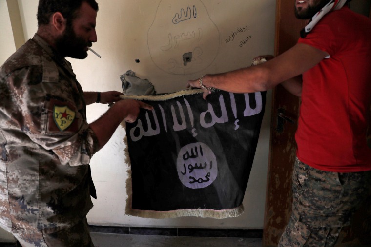 Image: Members of Syrian Democratic Forces hold a flag of the Islamic State militants recovered at a building next to the stadium in Raqqa