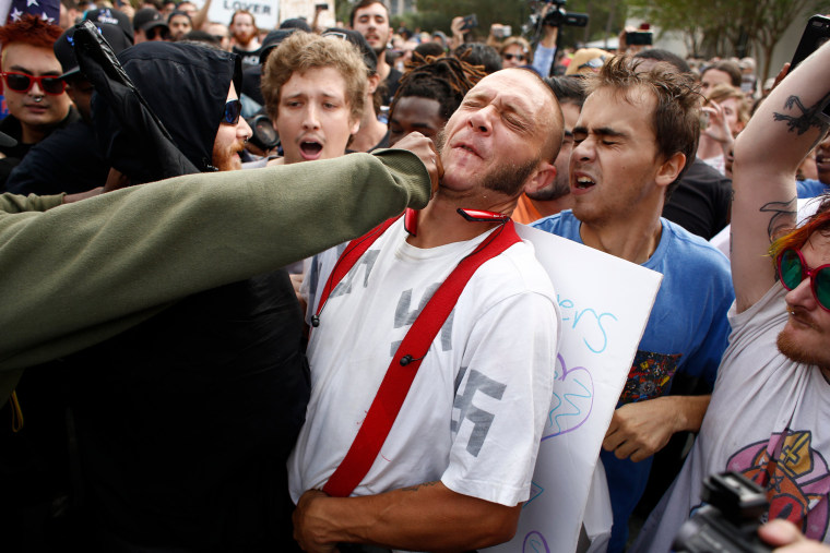 Image: A man wearing a shirt with swastikas is punched by an unidentified member of the crowd near the site of a planned speech by Richard Spencer