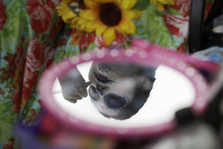 Image: A young woman gets her face painted in the style of Mexico's iconic Catrina ahead of the start of the parade.