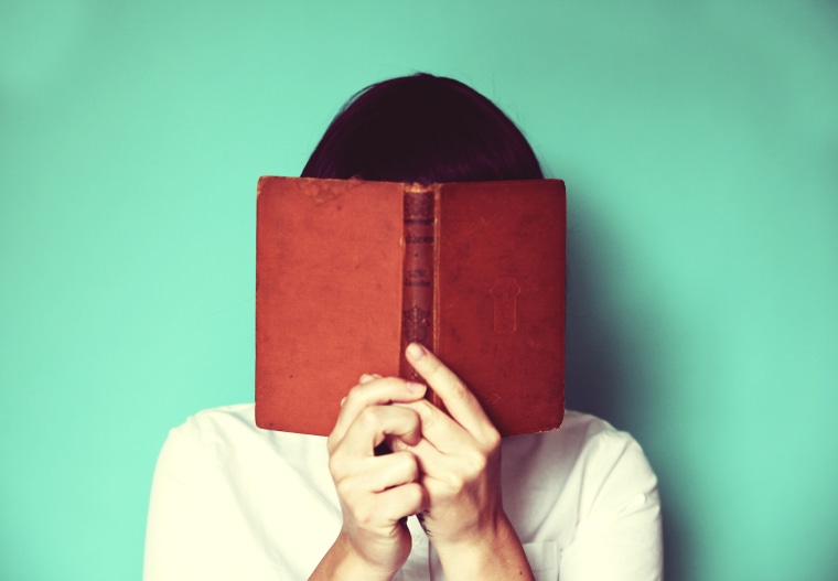Image: A woman holds a book in front of her face
