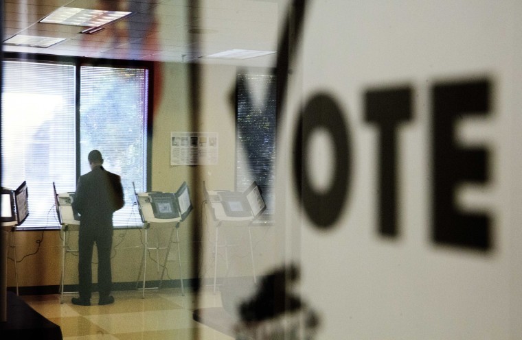 Image: A voter is reflected in the glass frame of a poster while casting a ballot during early voting in Atlanta