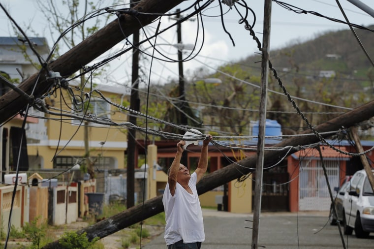 Image: A resident uses a plastic bag to move downed power cables so he can drive underneath them in a neighborhood that has not seen recovery efforts following Hurricane Maria in Ceiba