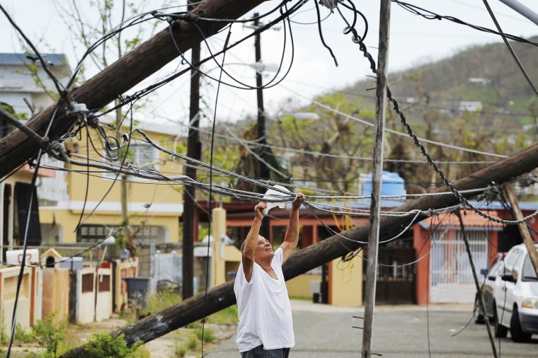 Image: A resident uses a plastic bag to move downed power cables so he can drive underneath them in a neighborhood that has not seen recovery efforts following Hurricane Maria in Ceiba