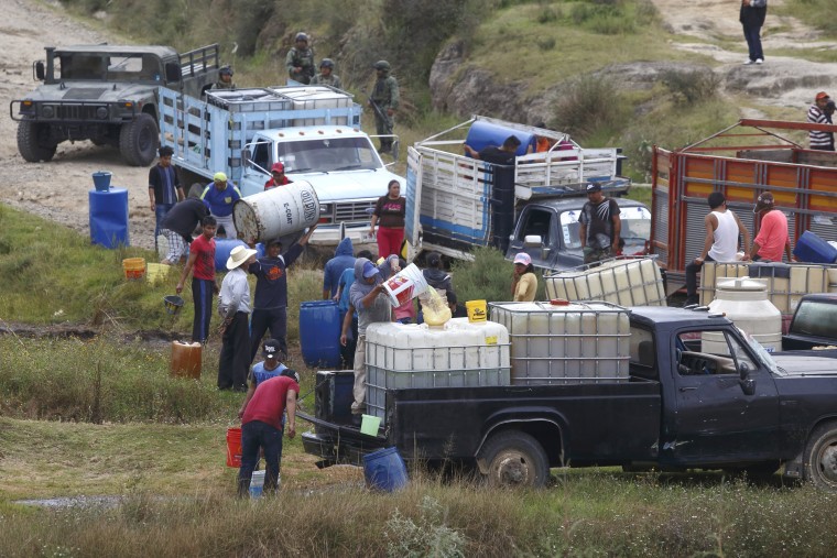 Image: People fill large drums of fuel from a clandestine outlet in San Francisco Tlaloc, Mexico