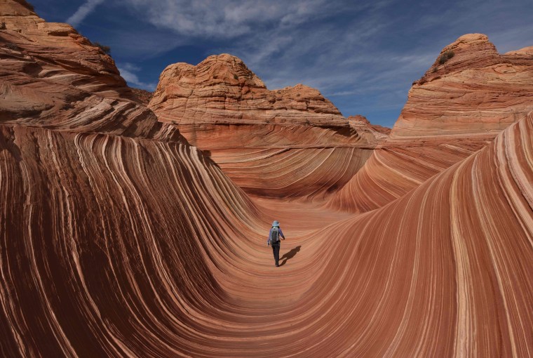 Image: A hiker walks through the U-shaped troughs of \"The Wave\" rock formation