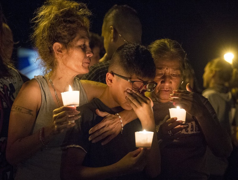 Image: Mona Rodriguez holds her 12-year-old son, J Anthony Hernandez, during a candlelight vigil held for the victims