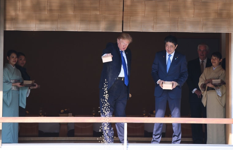 Image: Trump pours out the remaining fish food from a container as he feeds carp at a koi pond
